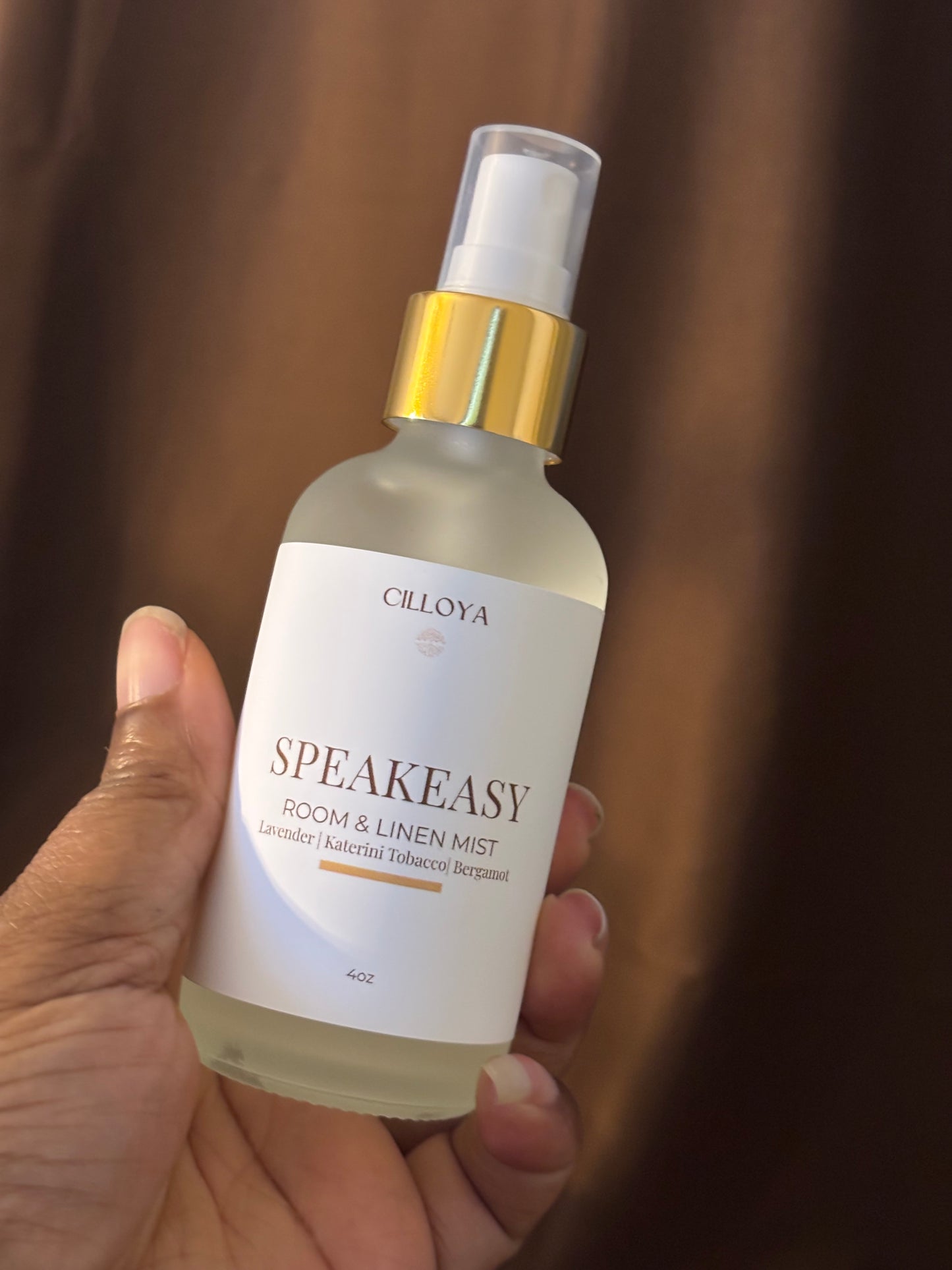 Hand holding a bottle of Cilloya Speakeasy room and linen mist against a blurred background.