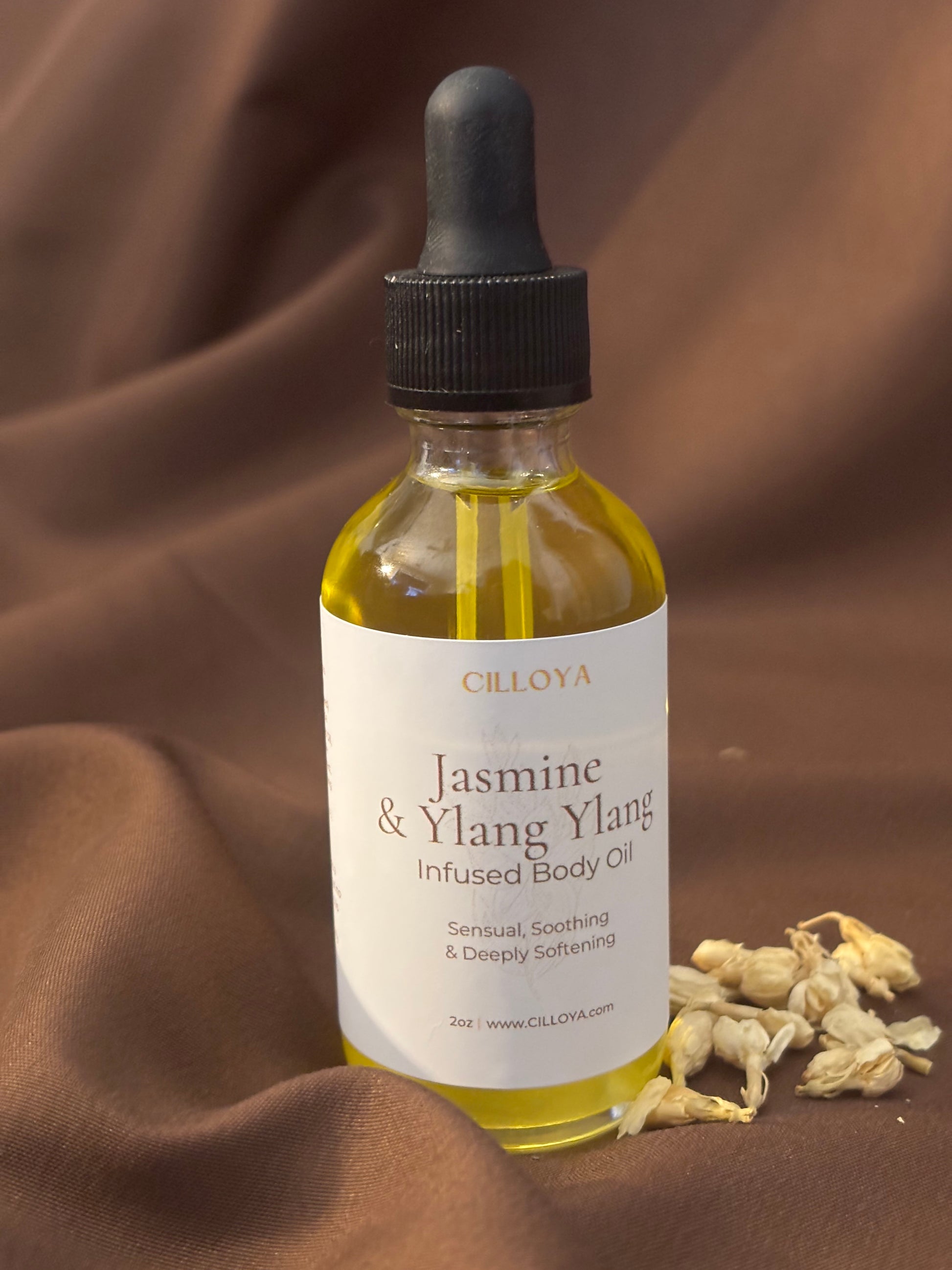 Cilloya Jasmine + Ylang Ylang Infused Body Oil in a 2oz clear glass dropper bottle with a black neck on a dark brown backdrop.