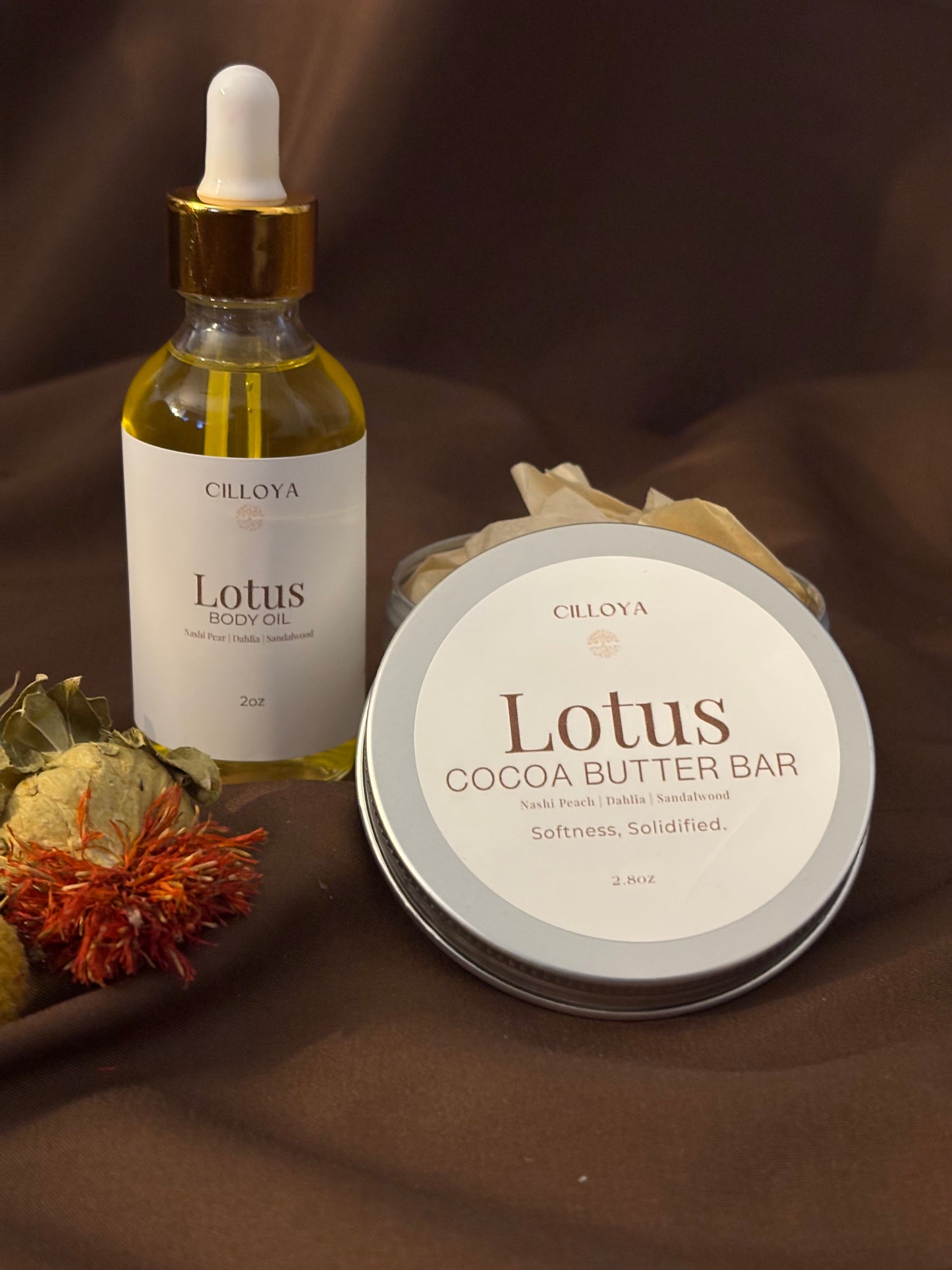 Cilloya Silk Experience gift set featuring a 2oz Lotus Body Oil and a 2.8oz Lotus Cocoa Butter Bar tin on a dark brown backdrop
