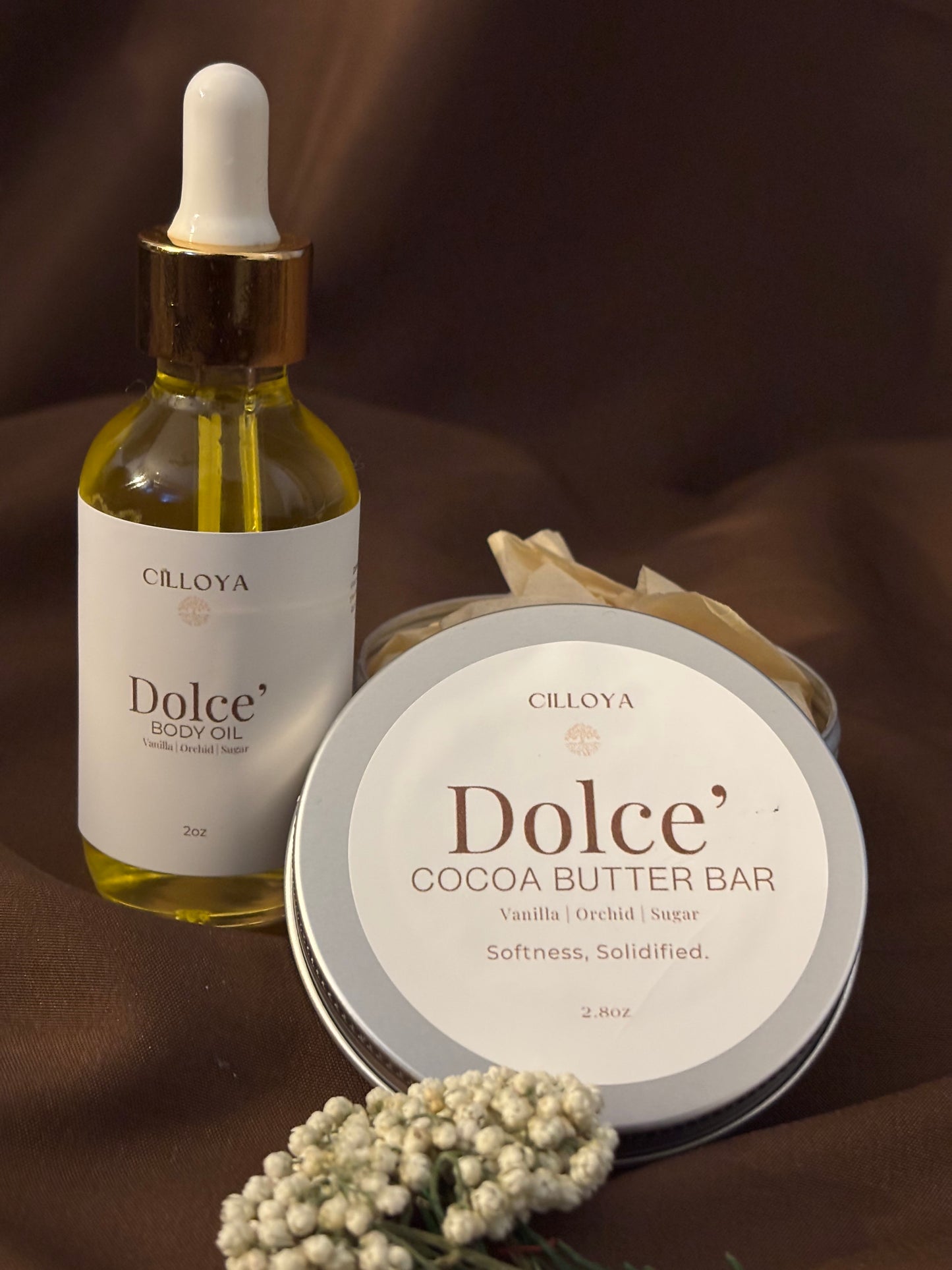 Cilloya Silk Experience gift set featuring a 2oz Dolce' Body Oil and a 2.8oz Dolce' Cocoa Butter Bar tin on a dark brown backdrop
