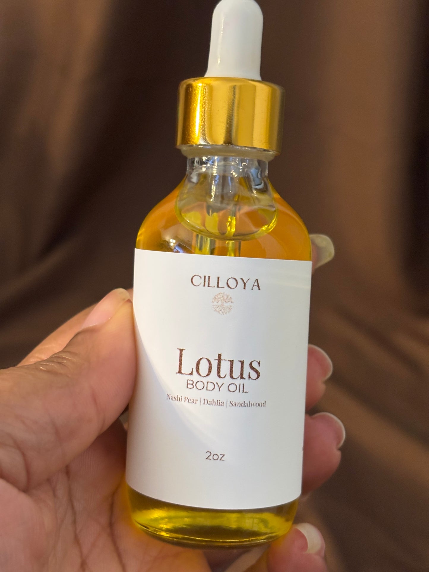 Cillova Lotus body oil bottle held in a hand with a dark brown background