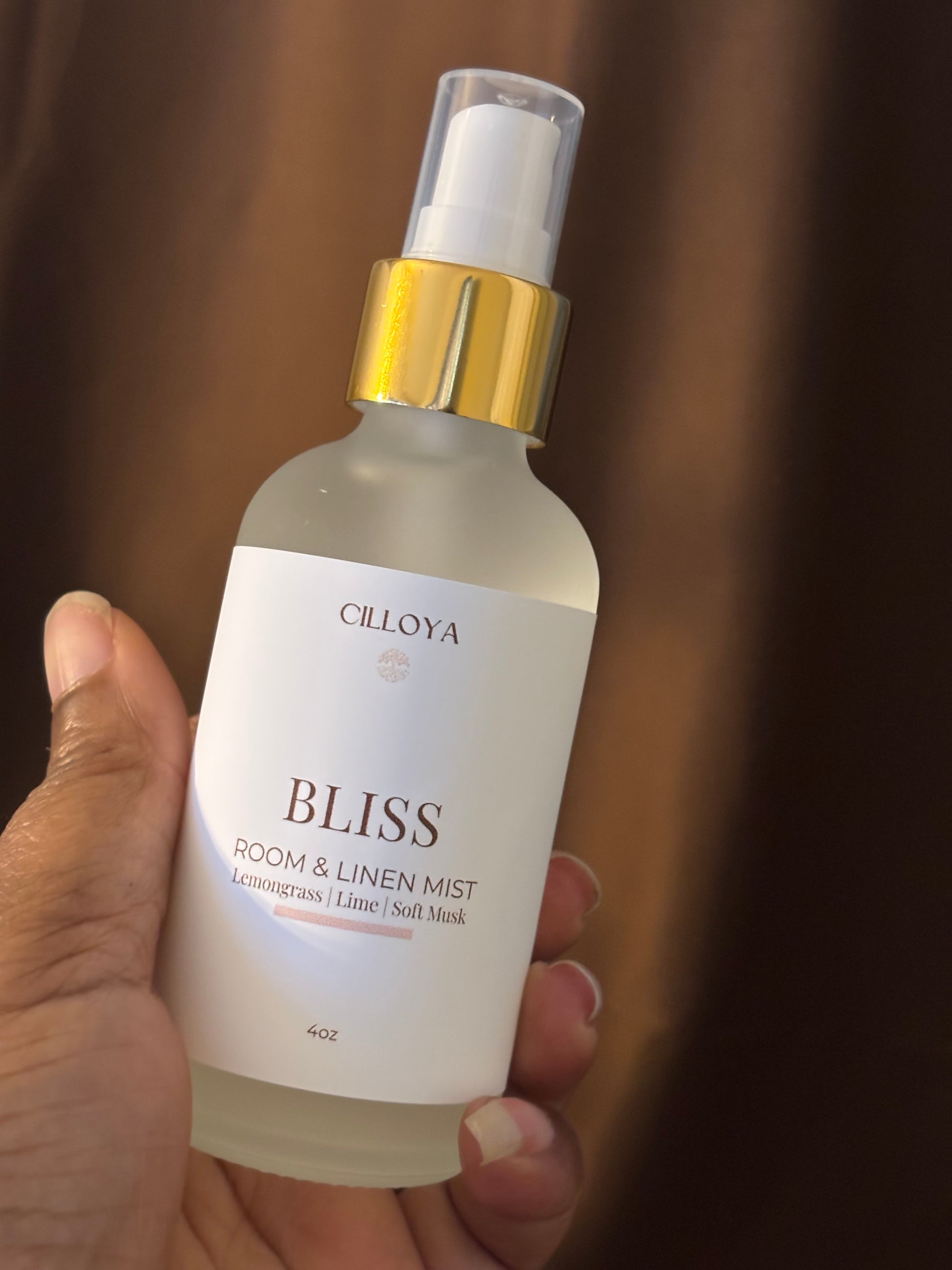 Cilloya Bliss room and linen mist bottle held by a hand against a dark brown background