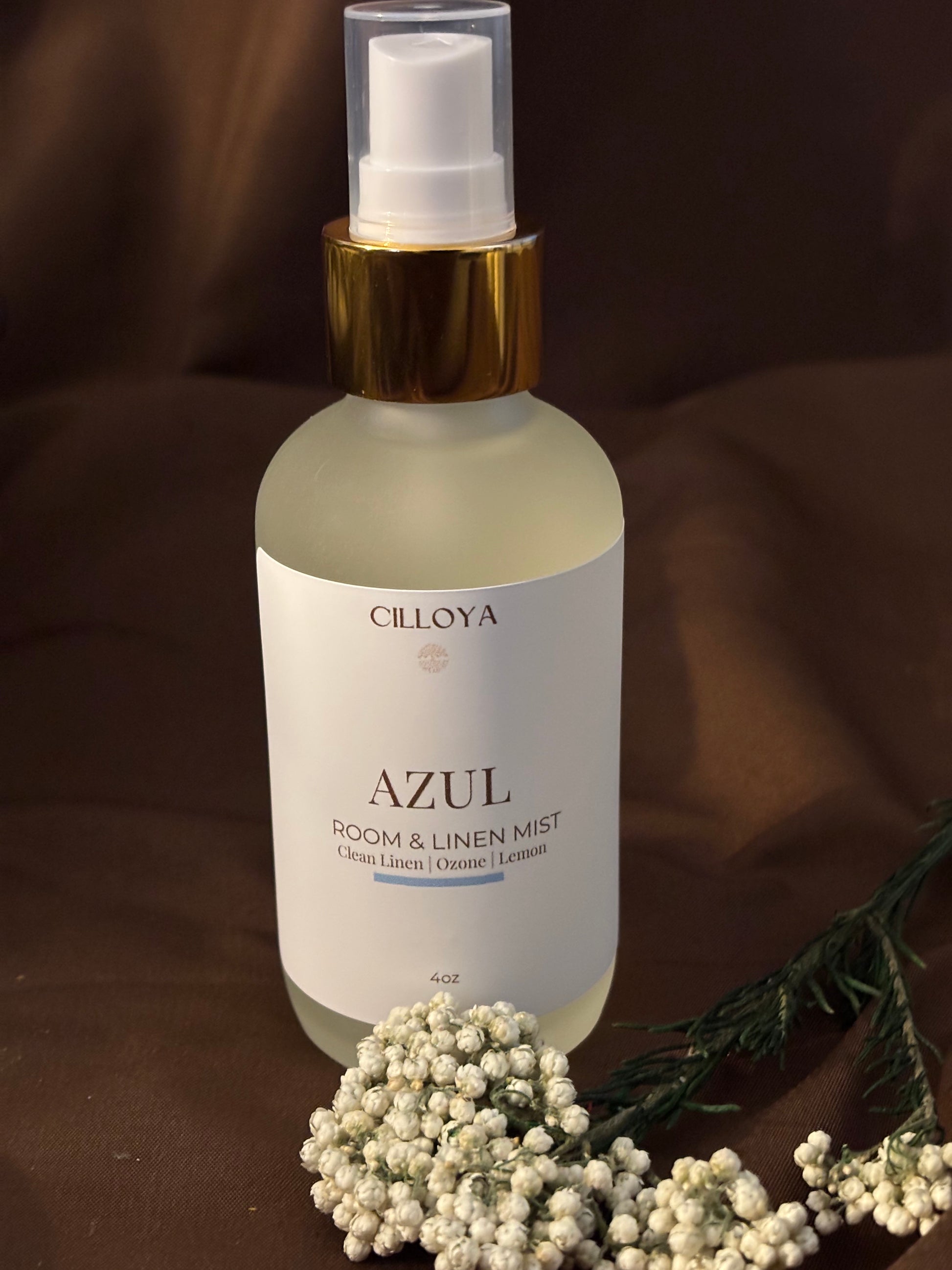 Cilloya Azul Room and Linen Mist in a 4oz frosted glass bottle with a gold neck, featuring notes of Linen, Ozone, and Lemon on a dark brown backdrop.