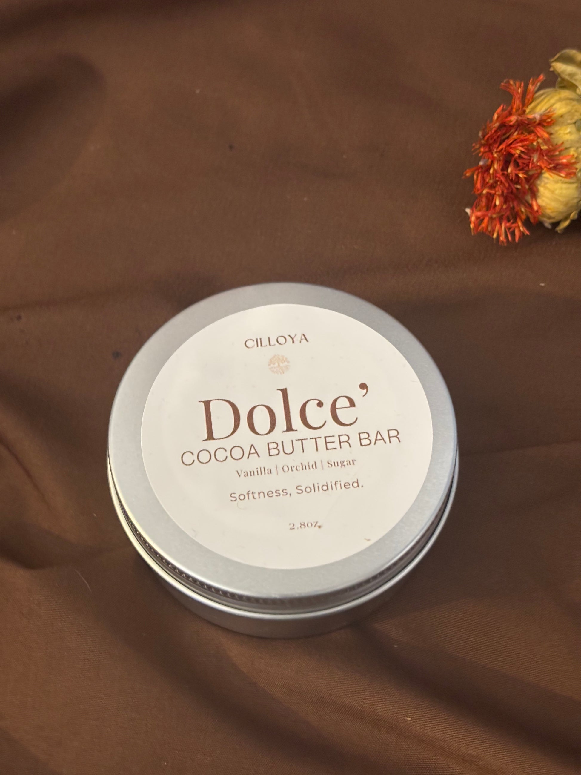 Cilloya Dolce' Cocoa Butter Bar round, silver tin container on a dark brown background with a flower.
