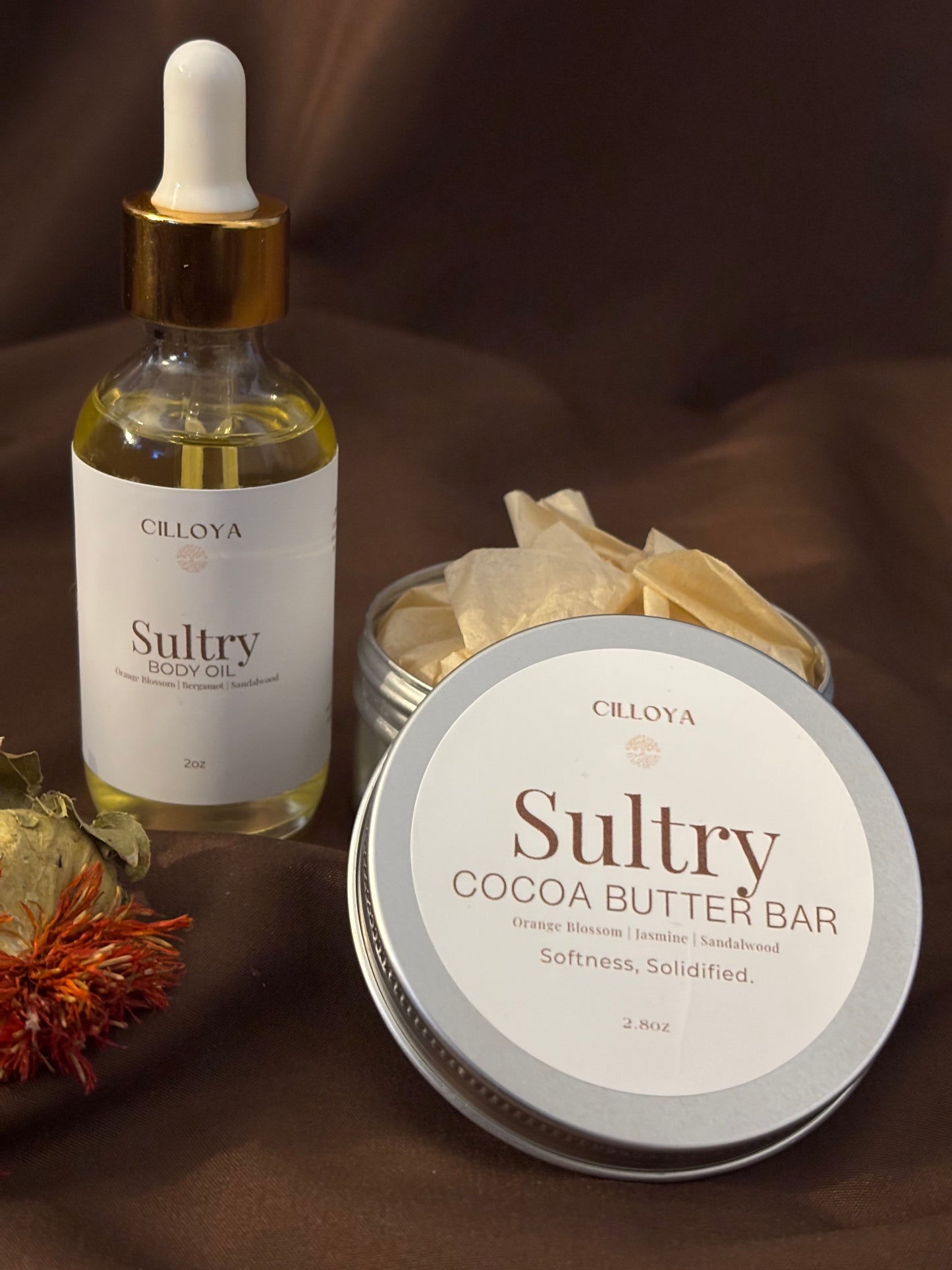 Cilloya Silk Experience gift set featuring a 2oz Sultry Body Oil and a 2.8oz 
Sultry Cocoa Butter Bar tin on a dark brown backdrop
