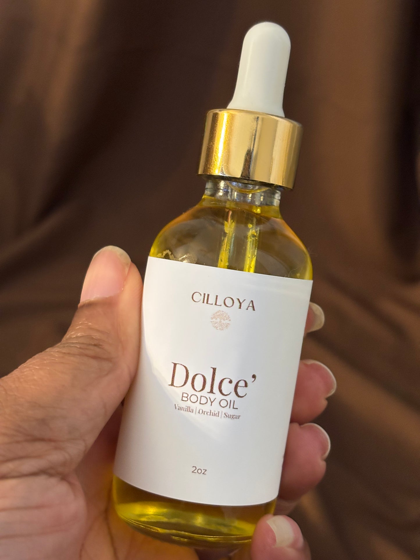 Bottle of Cillova Dolce' body oil held by a hand against a blurred background