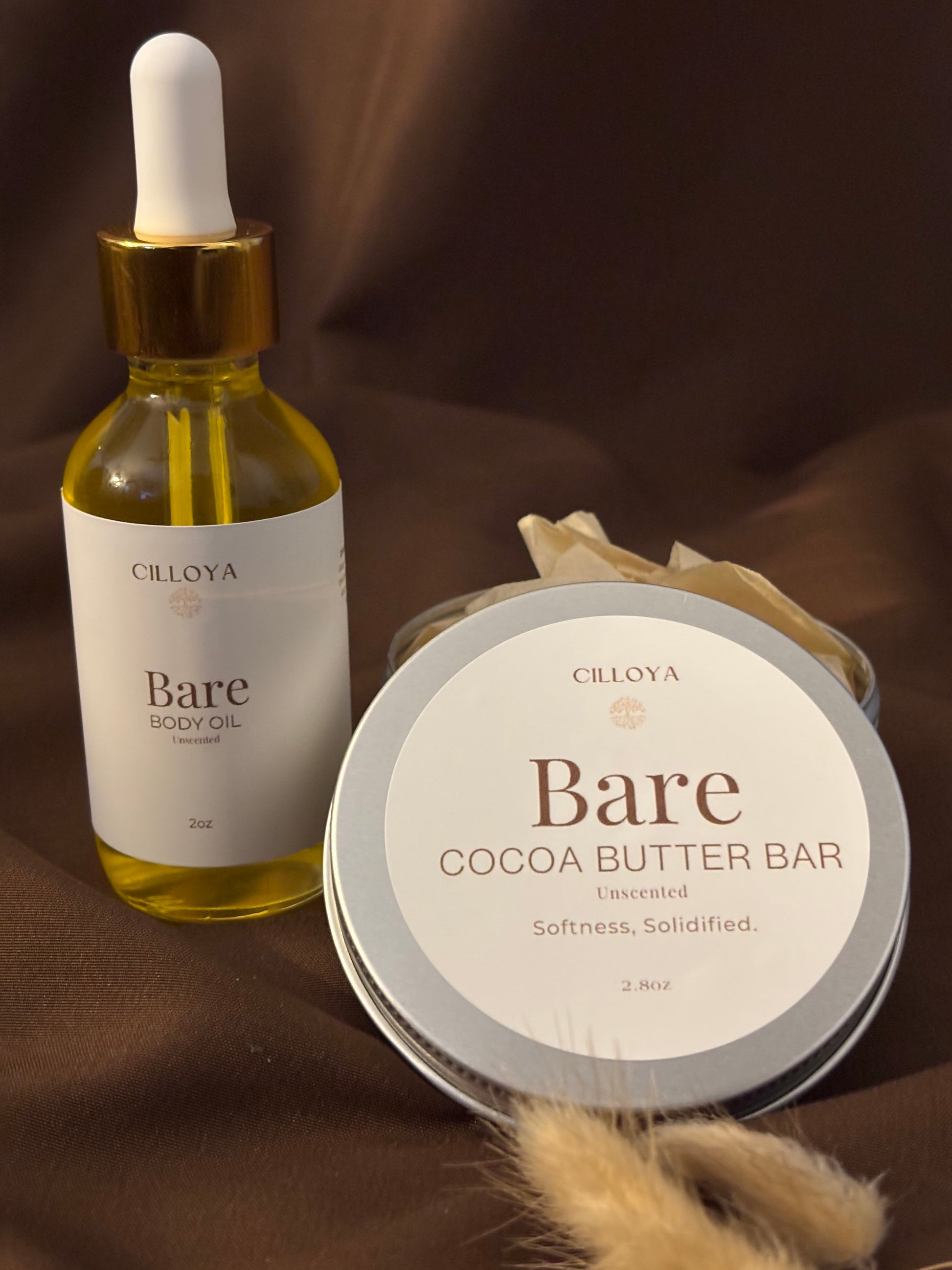Cilloya Silk Experience gift set featuring a 2oz Bare (Unscented) Body Oil and a 2.8oz Bare (Unscented) Cocoa Butter Bar tin on a dark brown backdrop