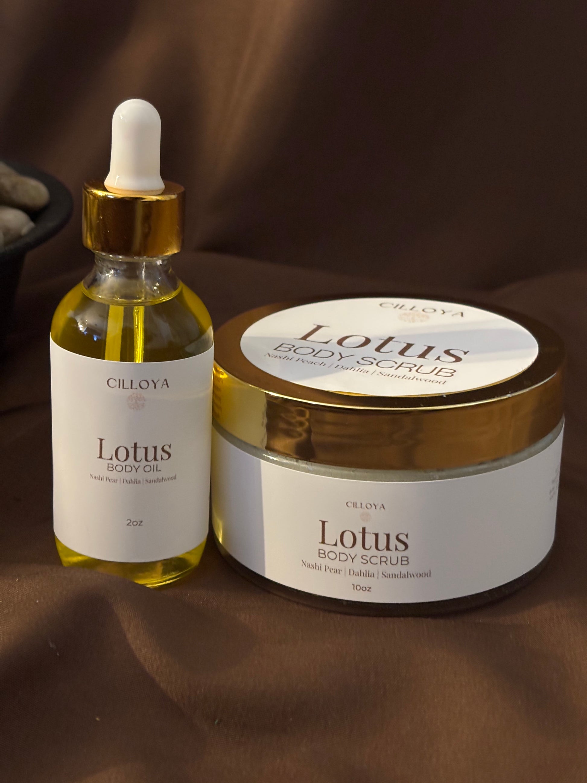 Cilloya Radiance Experience gift set featuring a 2oz Lotus Body Oil and a 10oz Lotus Body Scrub on a dark brown backdrop