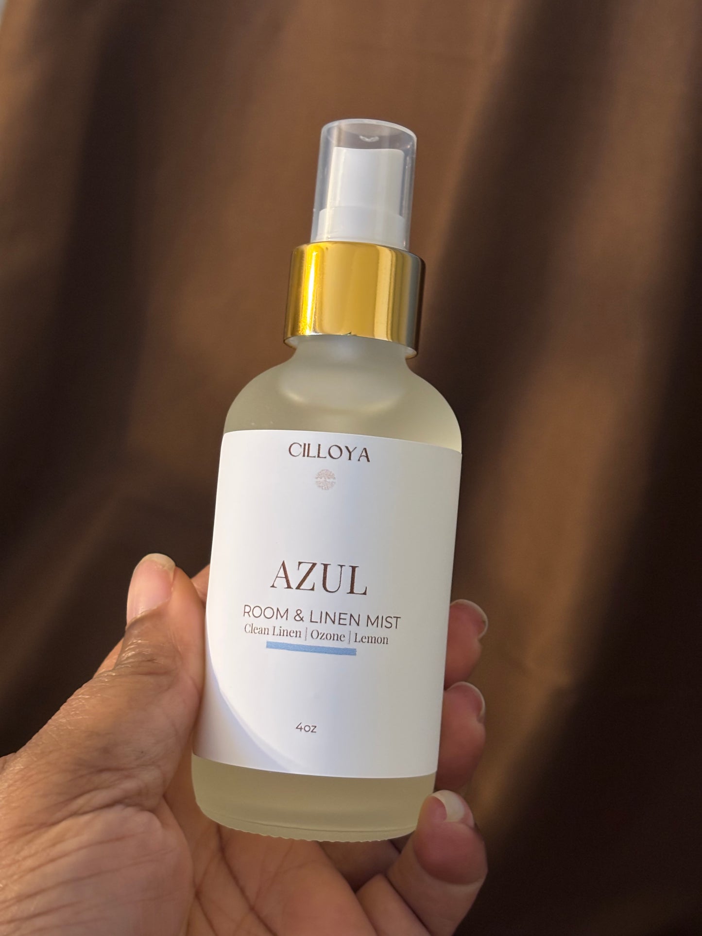 Hand holding a bottle of Cilloya Azul room and linen mist against a brown background