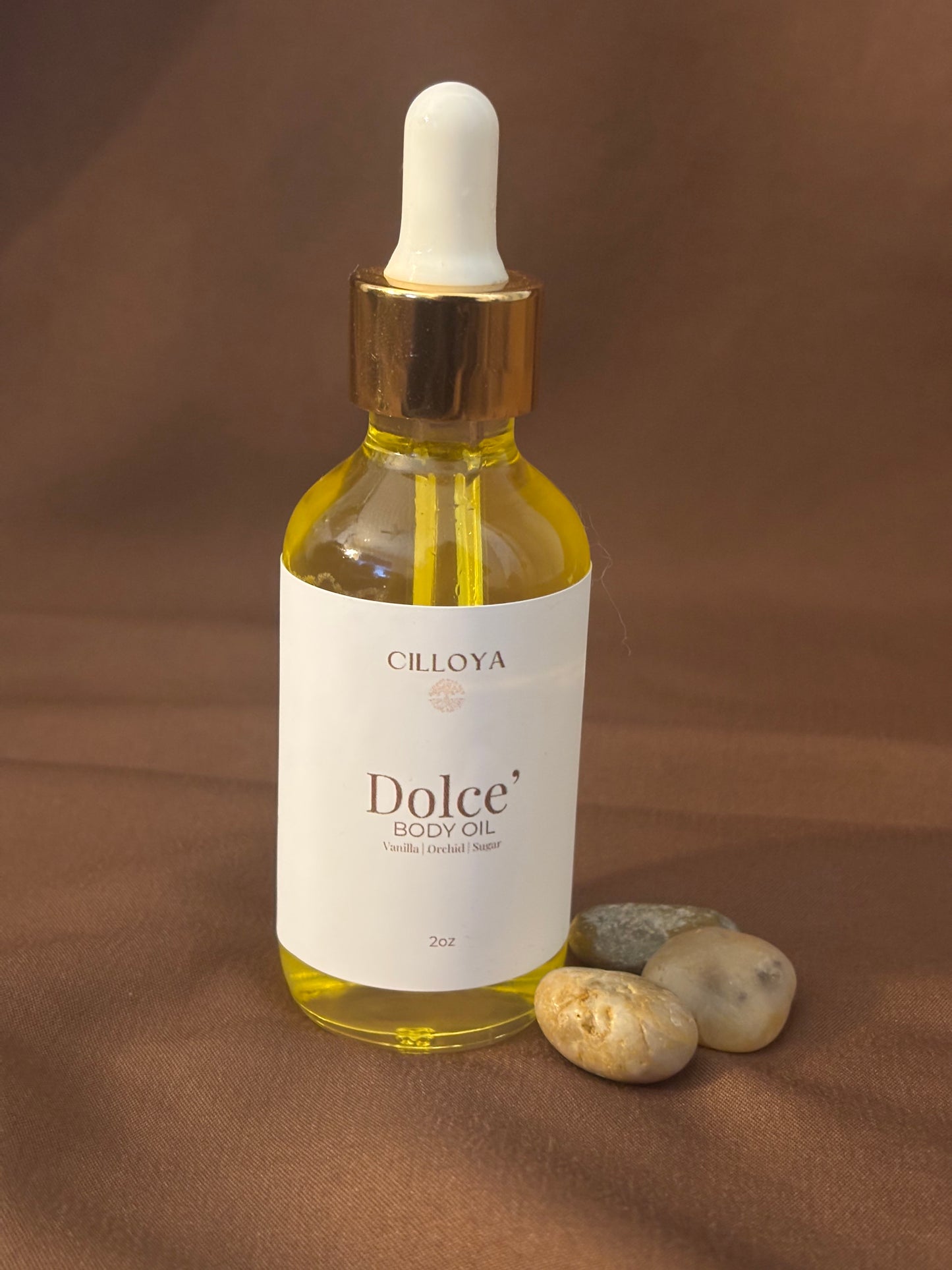 Cilloya Dolce Body Oil in a 2oz clear glass dropper bottle with a gold neck, featuring notes of vanilla, orchid and sugar on a dark brown backdrop
