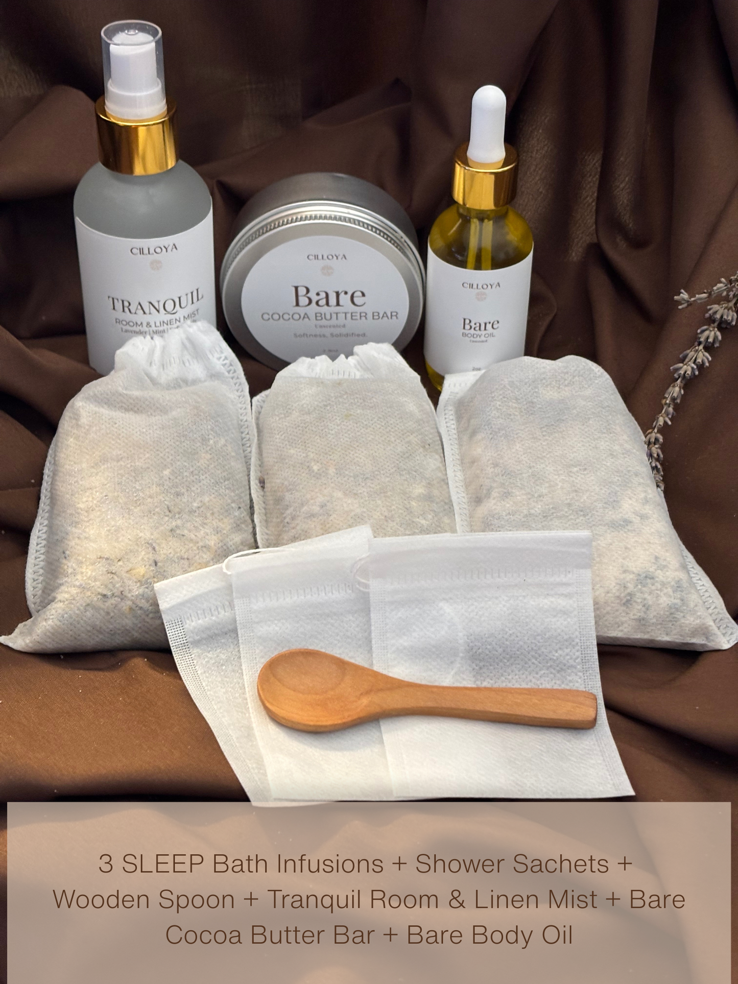 Cilloya Sanctuary Experience gift set arranged in three rows on a dark brown background: first row shows three small empty sachets fanned out with a wooden spoon resting diagonally across them; middle row shows three pre-filled Sleep bath and shower infusion sachets; last row shows Tranquil room and linen mist, a Bare Cocoa Butter Bar tin, and a 2oz Bare Body Oil bottle.
